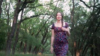 Saçları örgülü ve elbise giymiş güzel bir kadın yaz kenti parkında yürüyor.