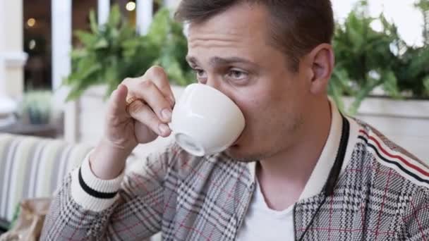 Porträtt av man i jacka närbild dricka kaffe i ett uteservering — Stockvideo