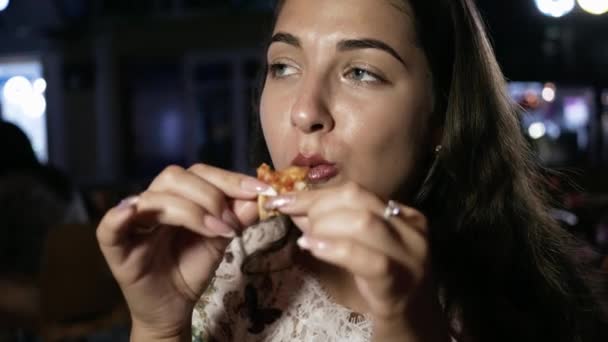 Retrato de una joven hermosa mujer que come pizza por la noche en la cafetería de la calle — Vídeo de stock