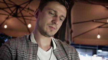 Genç adam bir sokak kafesinde menüye bakıyor. Gece geç saatlerde açık hava kapalı.