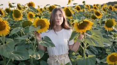 Genç, güzel bir kadın elinde iki ayçiçeğiyle poz veriyor.