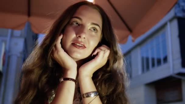 Portret van een jonge mooie vrouw in een café op straat in de avond — Stockvideo