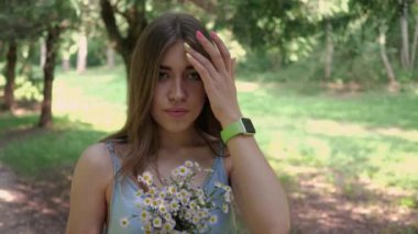 Küçük papatyaları olan genç bir kadın yaz parkında poz verir ve çiçekleri koklar.