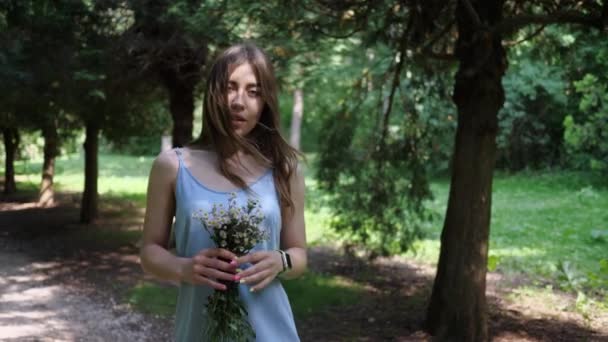 Junge Frau in blauem Kleid mit Strauß wilder Blumen im Park — Stockvideo