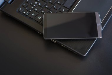 Siyah arka plan üstünde laptop ile akıllı telefon. Bir ofis için vazgeçilmez öğeleri