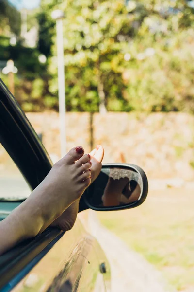 Girl with her feet out of the window of the car sunbathing on a