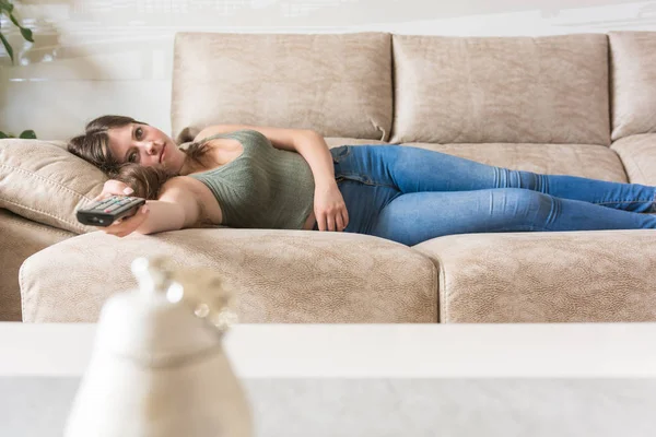 Девушка лежит на диване своего дома и смотрит телевизор. — стоковое фото