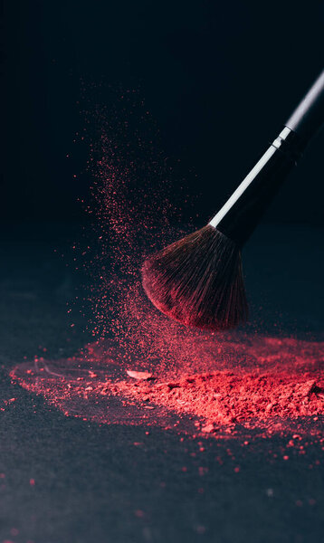 Make-up brush with violet powder explosion on black background