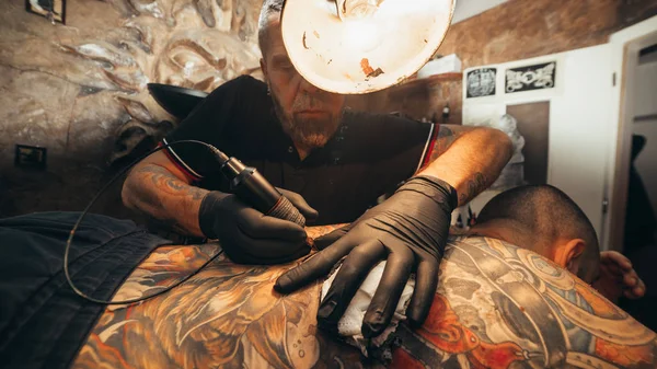 Close up of the tattoo machine. Tattooing. Man creating a picture on his back by a professional tattoo artist.