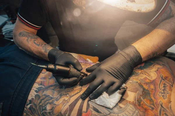 Close up of the tattoo machine. Tattooing. Man creating a picture on his back by a professional tattoo artist.