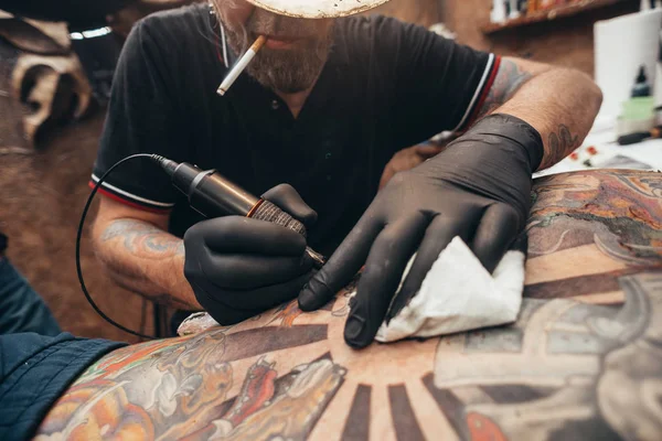 Close up of the tattoo machine. Tattooing. Man creating a picture on his back by a professional tattoo artist.