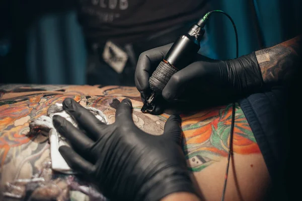 Close up of the tattoo machine. Tattooing. Man creating a picture on his back by a professional tattoo artist.