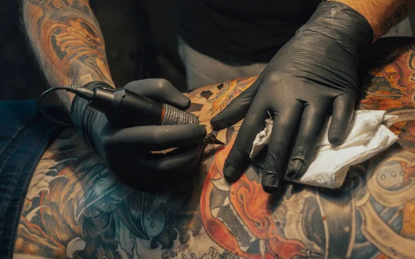 Close up of the tattoo machine. Tattooing. Man creating a picture on his back by a professional tattoo artist.