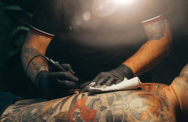 Close up of the tattoo machine. Tattooing. Man creating a picture on his back by a professional tattoo artist.
