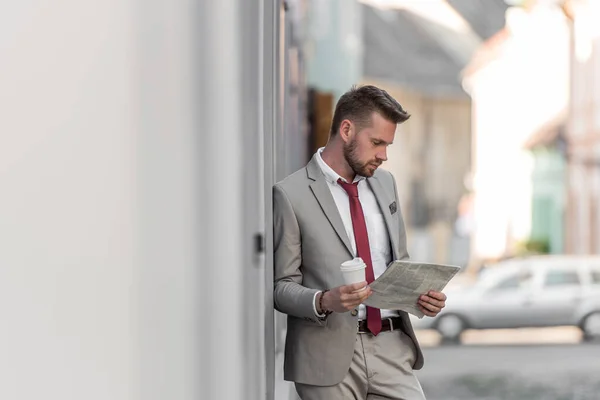 Portrait of a young businessman reading a newspapers and drinking coffee on the streets