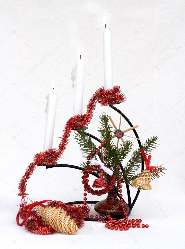fir branches with red christmas decorations and lit up candles on white background