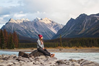 Genç kadın Gezgin pozlar arkasında, seyahat, İngiltere, Kanada Rocky Dağları nefes kesen bir arka plan ile nehir taşları üzerinde