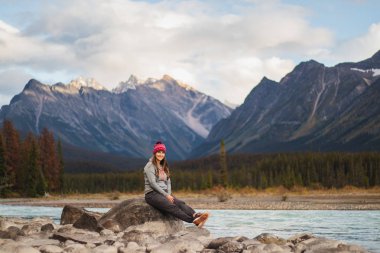 Genç kadın Gezgin pozlar arkasında, seyahat, İngiltere, Kanada Rocky Dağları nefes kesen bir arka plan ile nehir taşları üzerinde