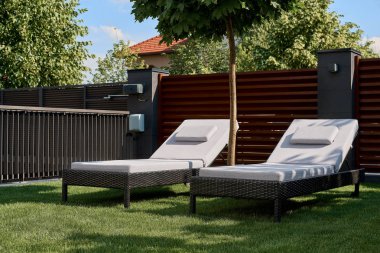 Evin avlusunda yeşil çim üzerinde iki şezlong vardır. Gevşeme, dinlenme, hafta sonu kavramı.