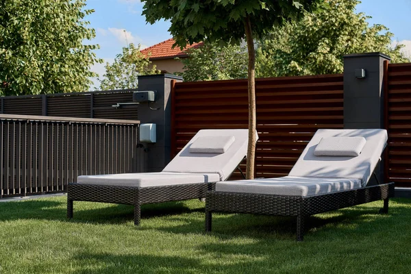 Evin avlusunda yeşil çim üzerinde iki şezlong vardır. Gevşeme, dinlenme, hafta sonu kavramı.