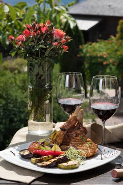 Romantik bir akşam yemeği dışında. bir iştah açıcı yemek domuz kaburga ve iki bardak kırmızı şarap, yeşil çim ve çiçek içinde belgili tanımlık geçmiş.