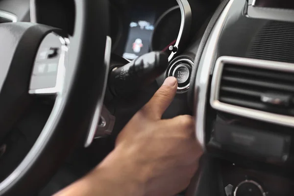 Finger pressing engine start button on car. The driver pushing on automatic start stop button.