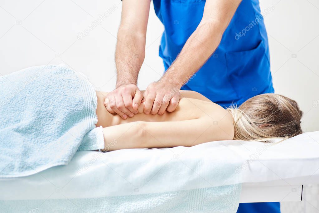 Physiotherapist doing healing treatment on man's back. Therapist wearing blue uniform. Osteopathy. Chiropractic adjustment, patient lying on massage table. Prevention of back treatment close-up.