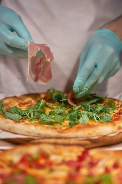 Şef ellerini et koyarak yakın bir görünüm de bir parma veya prosciutto jambon İtalyan pizza yapma. seçici odaklama.