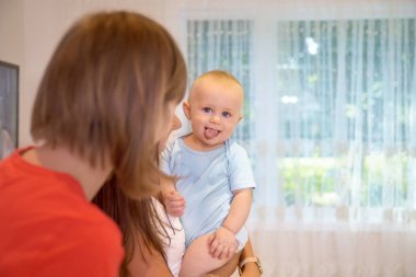 Neşeli anne oğlu ile kanepede bulundukları oynarken keyif alıyor. O çocukla eğlenceli parmakları işaret ediyor ve küçük çocuk ona heyecanla izliyor. Anne ve oğlu evde, mutlu bir aile oynamak