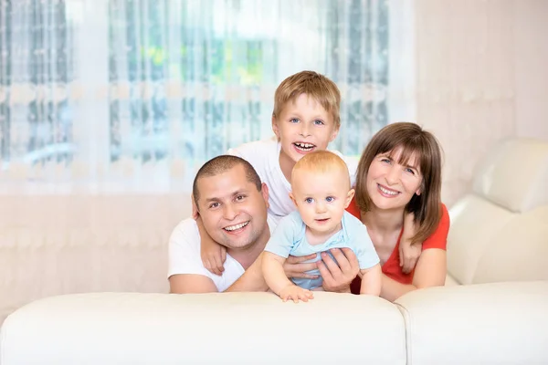 El concepto de la familia, padres jóvenes con un bebé y su hermano, la infancia feliz. La familia en el sofá está mirando a la cámara, sonriendo. una familia feliz — Foto de Stock