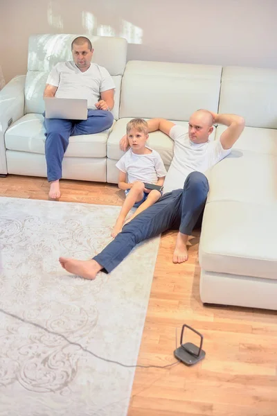 Молодая семья смотрит телевизор, два парня и маленький мальчик сидит на диване и пол в гостиной на дому — стоковое фото