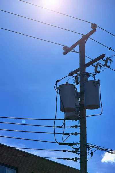 Energy and technology: electrical post by the road with power line cables, transformers against bright blue sky providing