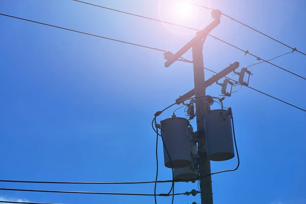 Energy and technology: electrical post by the road with power line cables, transformers against bright blue sky providing