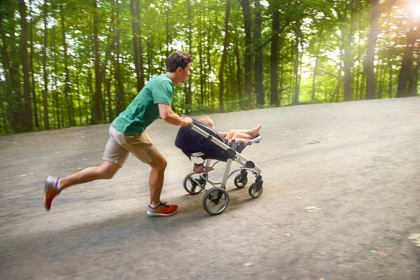 brother with a stroller runs on a walk in the park with a little girl in a stroller under the sunset sunlight. Play with the kids