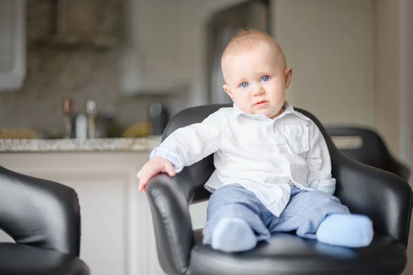 Primer plano retrato de adorable niño sentado en la silla, mirando directamente a la cámara, pelo rubio, ojos azules. Tiro de interior en la cocina —  Fotos de Stock
