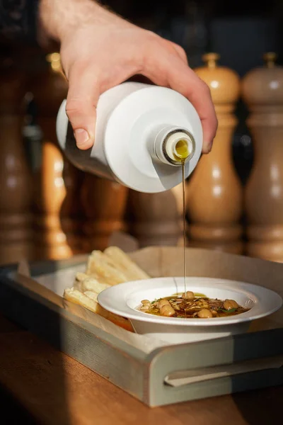 Snack tradicional mediterráneo. Cocine vierte aceite de oliva en un hummus con piñones, aceite de oliva, servido en un plato con pan de pita, servido en un restaurante . — Foto de Stock