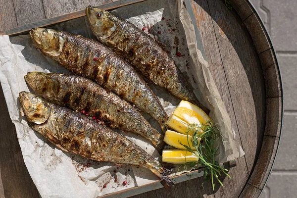 Grilled mackerel fish with baked vegetables on a wooden tray in the street, terrace, outdoor cafe, sunset. — Stock Photo, Image