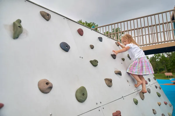Little child girl trying on free climbing on the playground wooden wall. — Stock Photo, Image