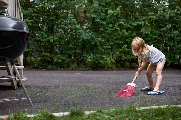 Little girl helps her parents collect grass in the yard. Seasonal gardening. Cleaning the yard
