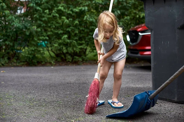 Little girl helps her parents collect grass in the yard. Seasonal gardening. Cleaning the yard