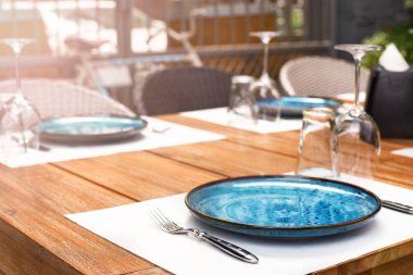 Güneşlenme terasında kahvaltı masası. Masada mavi tabak, restoranda ziyaretçi bekliyor.