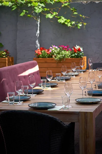 Gran mesa en la terraza para los huéspedes. Platos azules y vasos sobre la mesa para los visitantes del restaurante. De cerca. —  Fotos de Stock