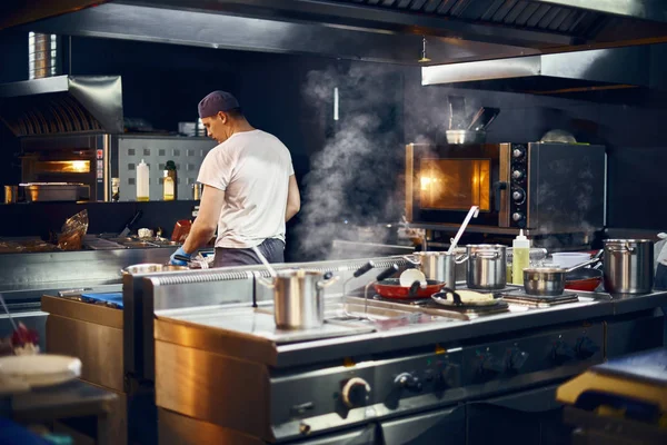 Cook stands with his back, Cooking in a modern kitchen, in a restaurant. low key. Copy space for text — Stock Photo, Image