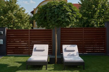 Evin avlusunda yeşil çim üzerinde iki şezlong vardır. Gevşeme, dinlenme, hafta sonu kavramı