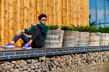 Önlükteki genç adam ahşap bir evin terasında oturuyor. Sarı tahta. Panoramik pencereler. Mavi gökyüzü penceresinde mükemmel yansıma.