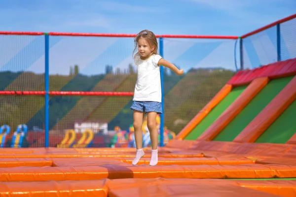 Niña bonita divirtiéndose al aire libre. Saltar sobre trampolín en zona infantil. Chica feliz saltando en el trampolín amarillo en el parque de atracciones — Foto de Stock