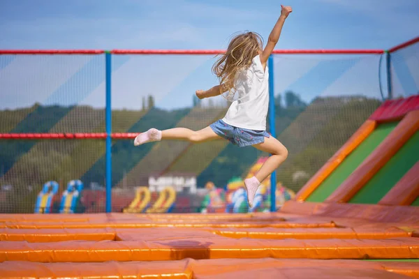 Menina bonita se divertindo ao ar livre. Saltando em trampolim na zona infantil. Menina feliz pulando no trampolim amarelo no parque de diversões — Fotografia de Stock