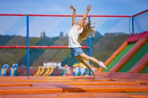 Little pretty girl having fun outdoor. Jumping on trampoline in children zone. Happy girl jumping on the yellow trampoline in Amusement park — Stock Photo, Image