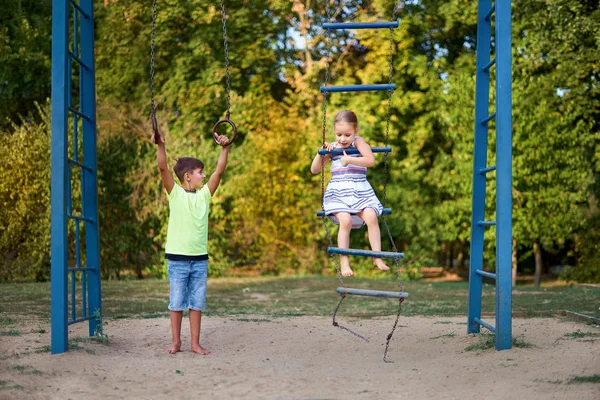 Duas crianças sorridentes felizes estão se exercitando em um campo de esportes. Irmão e irmã alegres praticam esportes juntos. Miúdos felizes a divertir-se no relvado do parque. Dia das crianças — Fotografia de Stock