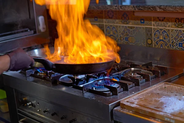 Concepto de comida. El chef fríe en una sartén los tomates y las ostras, preparando un plato una sartén cubierta de llamas. El proceso de cocción de espaguetis con mariscos — Foto de Stock